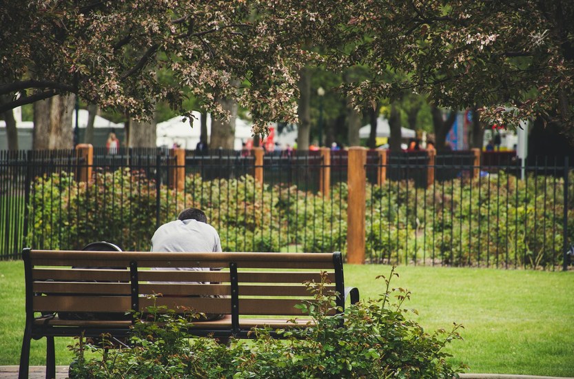 Person sitzt nachdenklich auf einer Bank und schaut in die Ferne