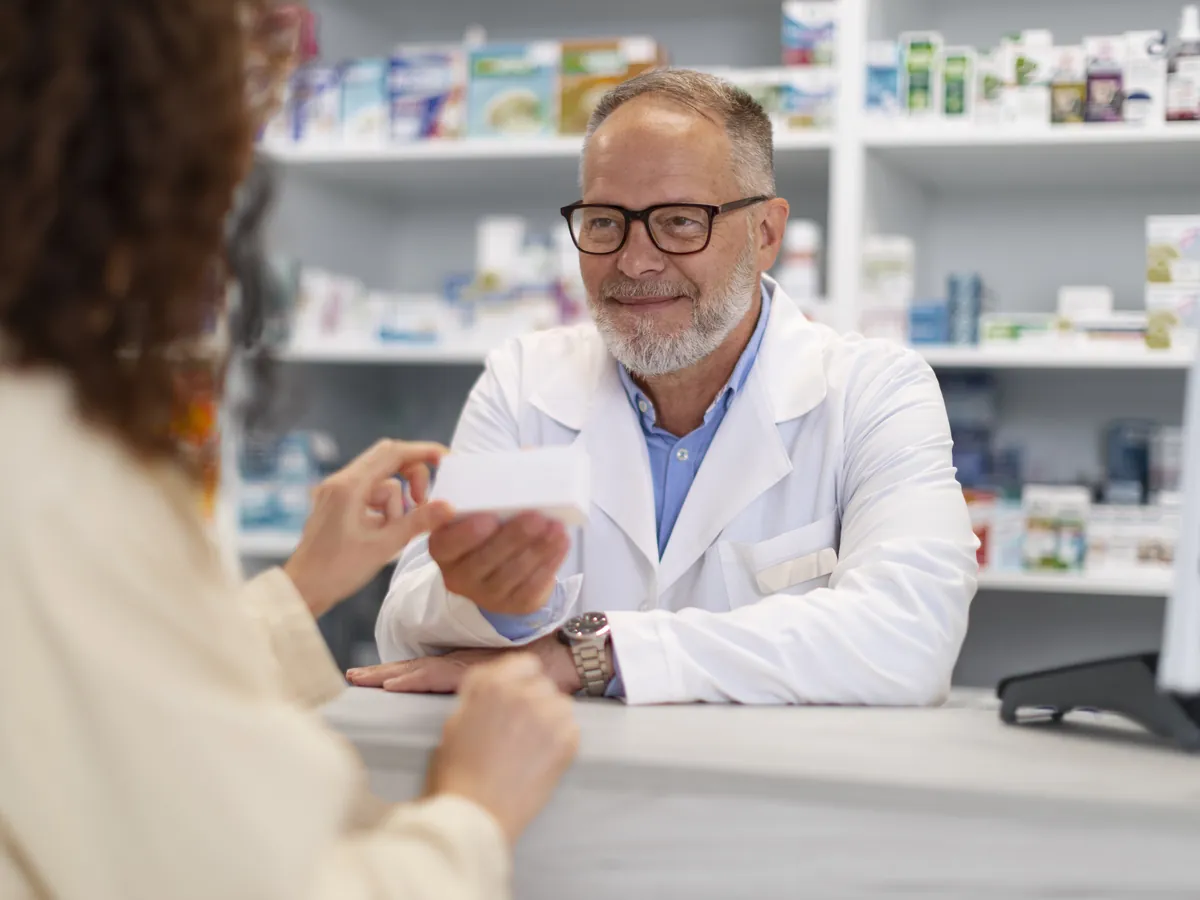 Apotheker übergibt einer Kundin ein verschreibungspflichtiges Medikament über den Tresen