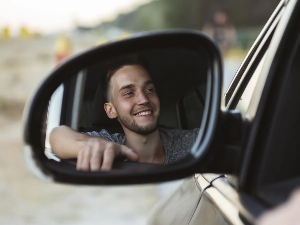 Junger Mann lächelt im Außenspiegel seines Autos, nachdem er nach der MPU wegen Cannabis den Führerschein zurückbekommen hat
