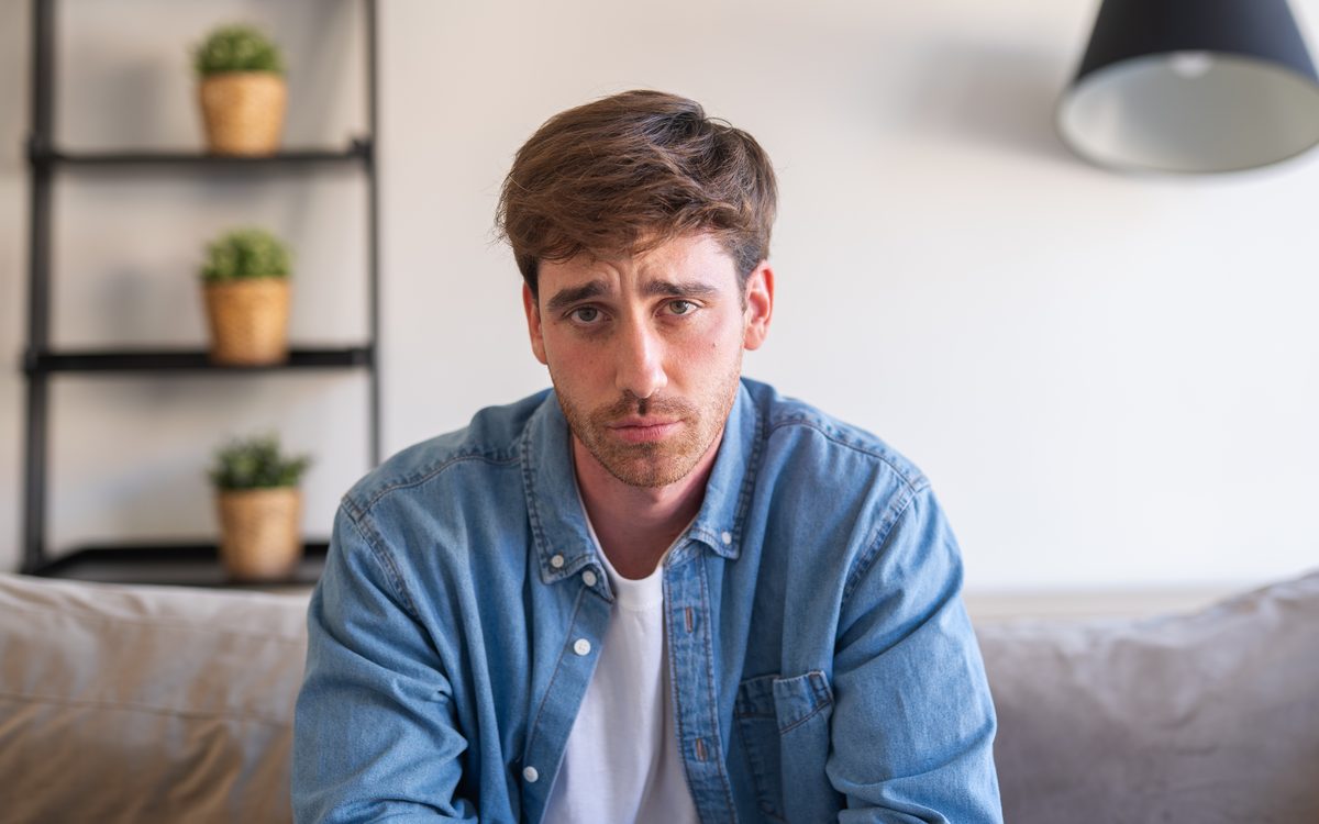 Junger Mann sitzt nachdenklich auf dem Sofa